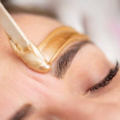 Applying Gold Colored Wax with Spatula on Woman's Face